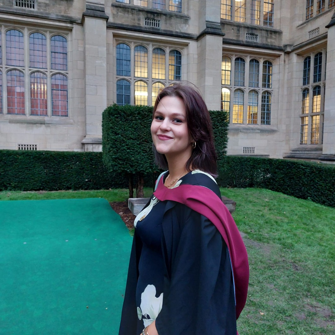 Law graduate Georgie Lockwood atending in her graduation gown outside the university buildings
