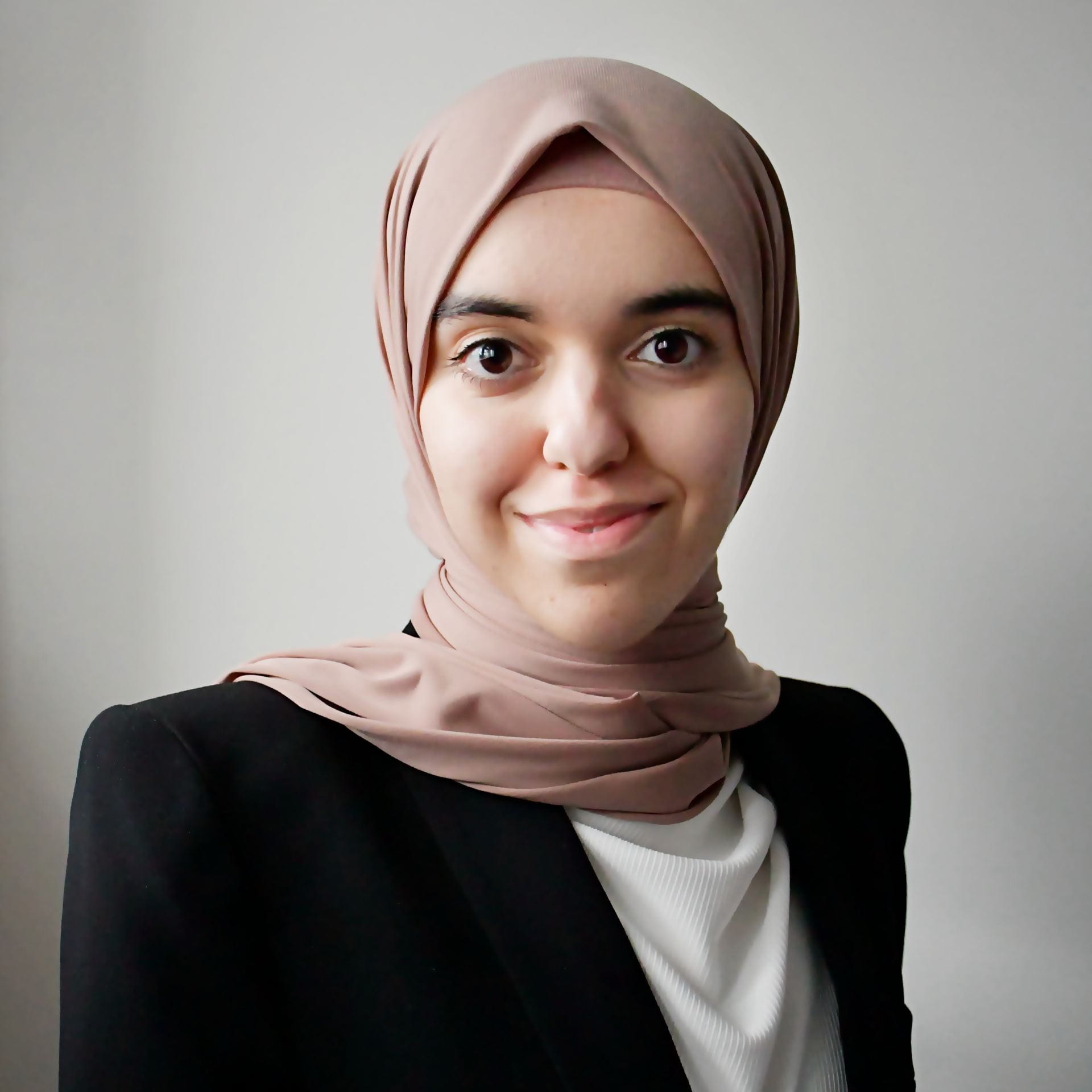 Smiling image of law student, Nafisa El-Turke looking into the camera wearing a smart dark suit jacket, white blouse and pale pink headscarf.